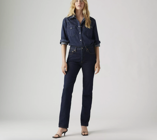 Woman wearing a dark denim shirt and jeans on a plain background