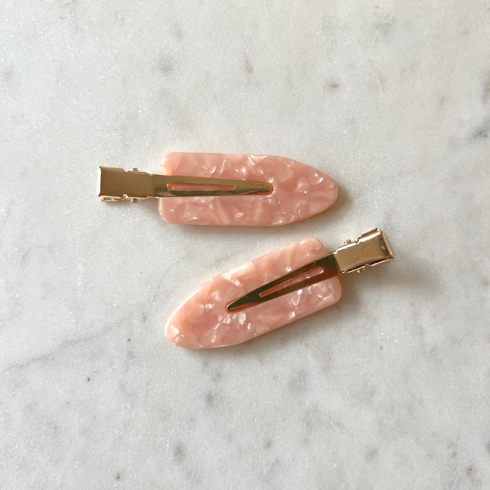 Two pink hair clips with gold clips on a marble surface