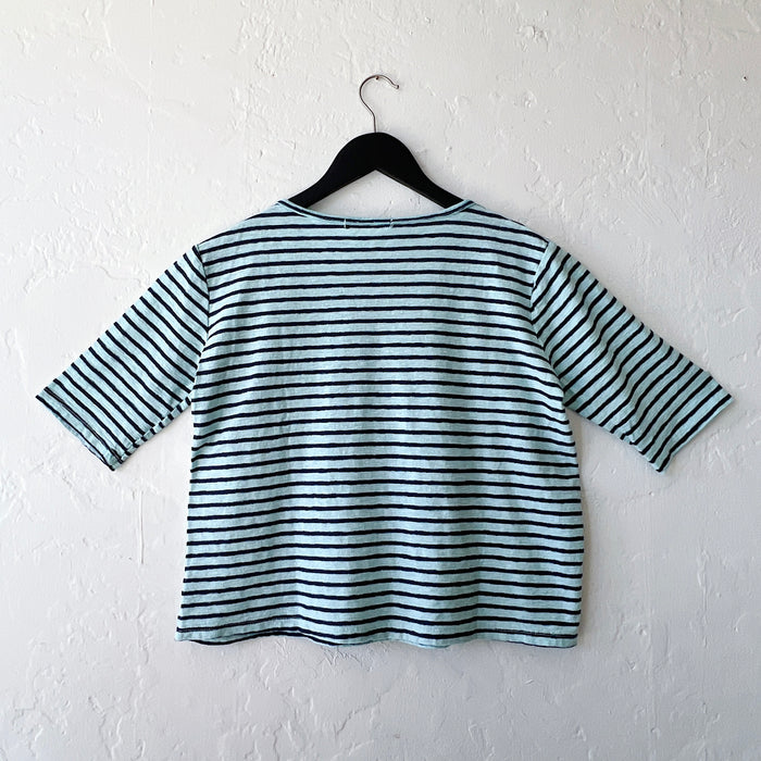 Blue and black striped shirt on a hanger against a white wall, viewed from behind