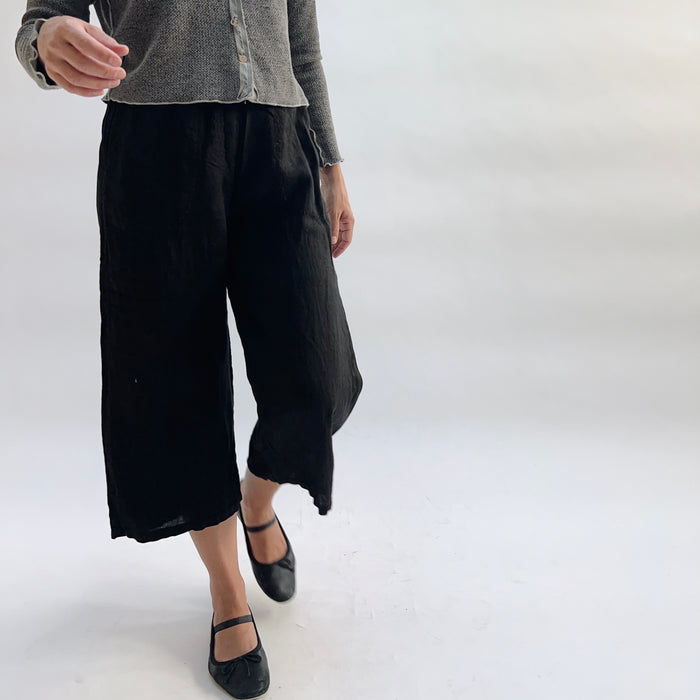 Cut Loose Hanky Linen Easy Crop Flood Pant in Black, black 100% linen wide-leg crop pant in motion, styled with a grey button-front cardigan and black Mary Jane flats — angled front view showing movement and side vent hem