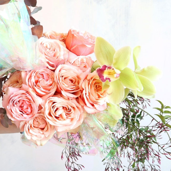 Peach roses, green orchids, greenery, and iridescent plastic.